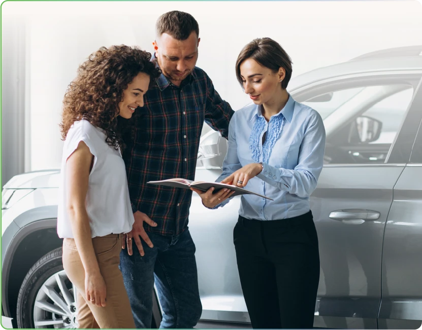 a couple going through a brochure with a saleswoman in front of a silver suv