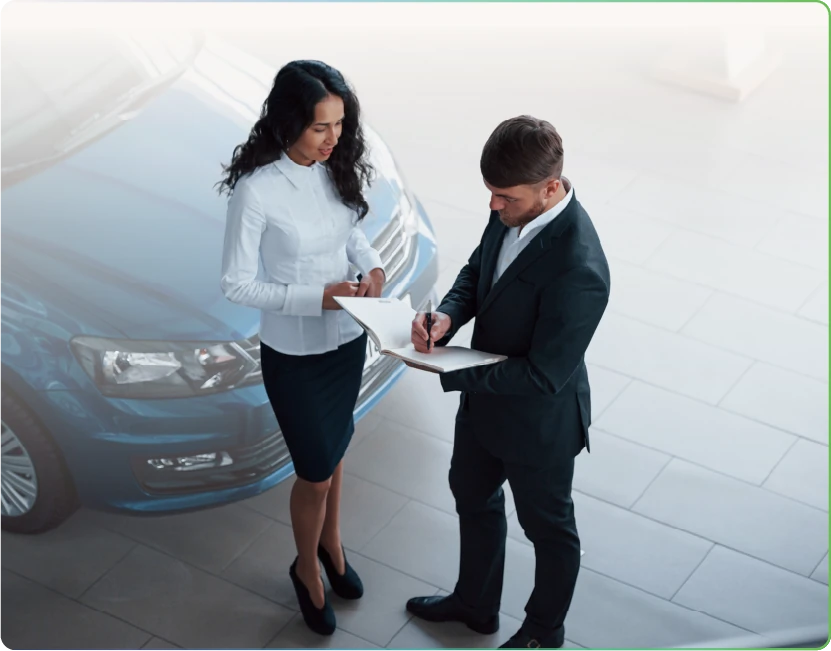 a salesperson and a customer signing paperwork beside a blue car in a showroom